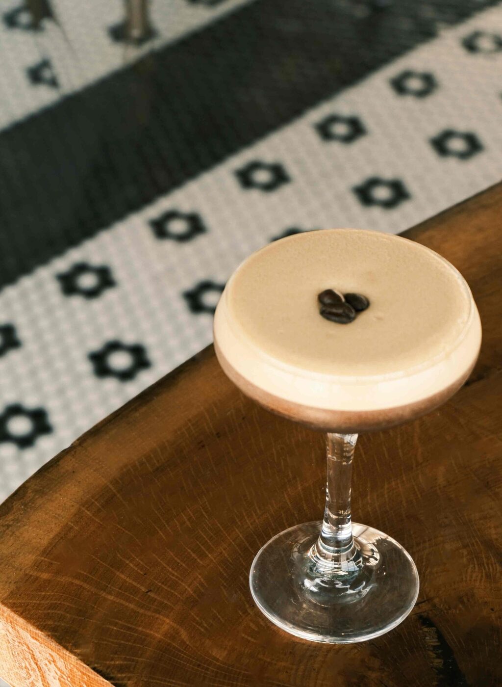 Bai-tee espresso martini topped with three coffee beans on a reclaimed wood bar
