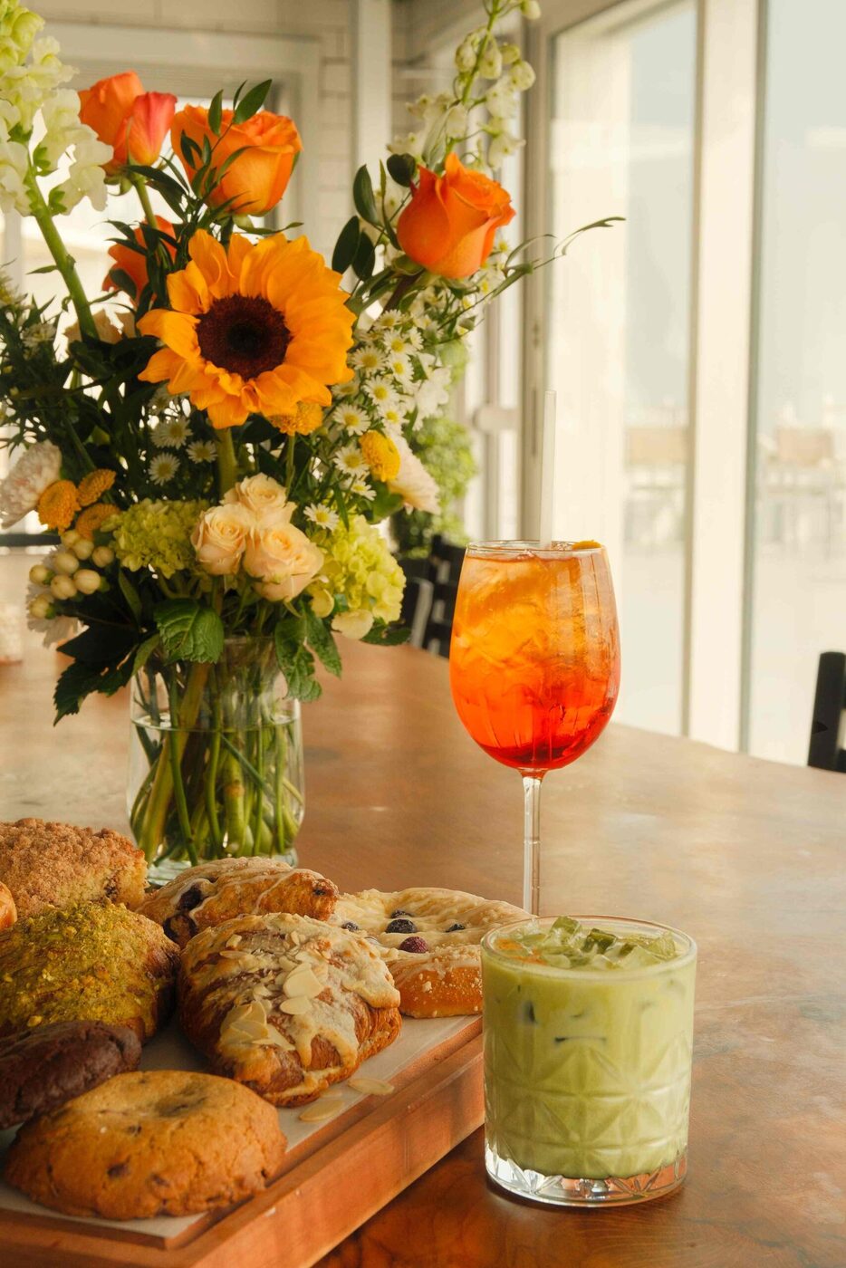 Aperol spritz and iced matcha beside fresh morning pastries and flowers at bai-tee