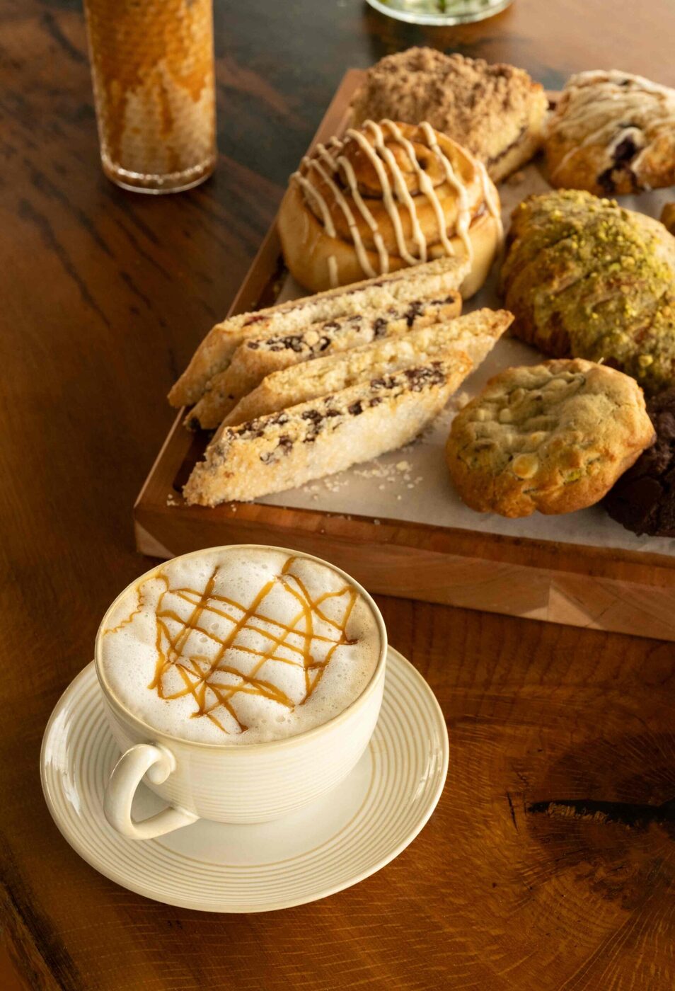 Caramel latte art beside a board of house biscotti and morning pastries at bai-tee