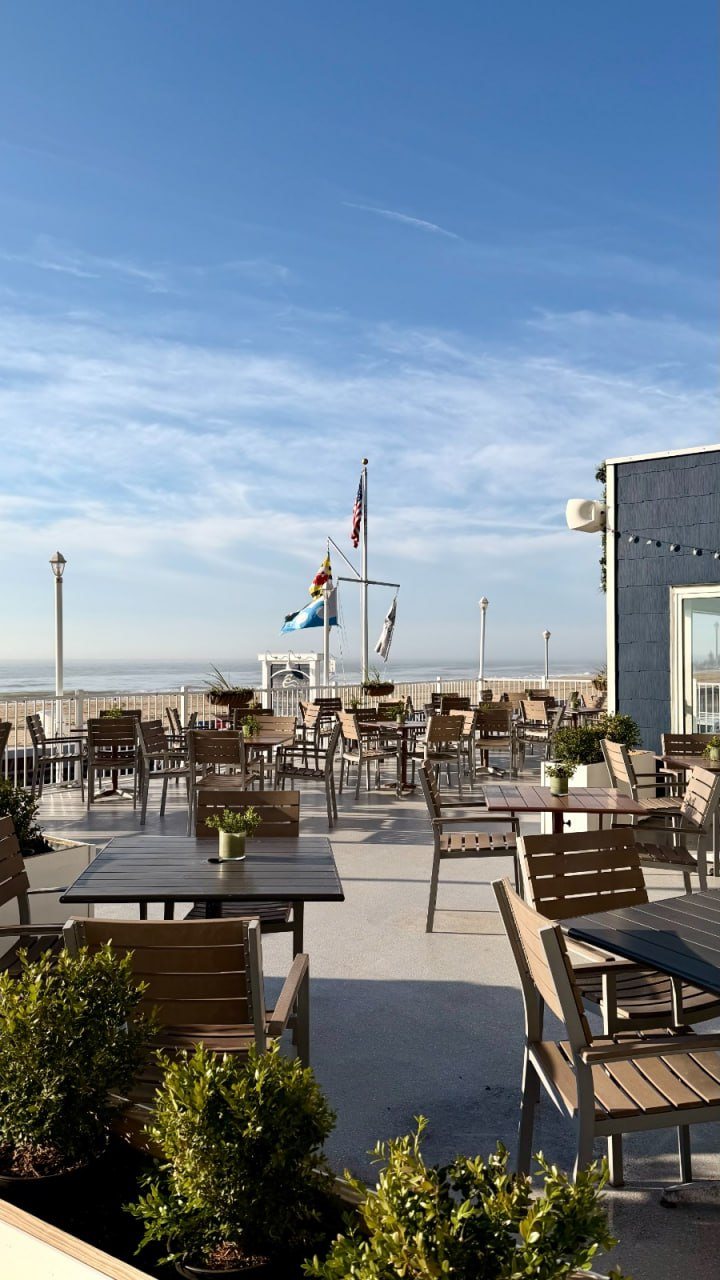Beachfront patio tables at bai-tee with flags flying and the Atlantic beyond