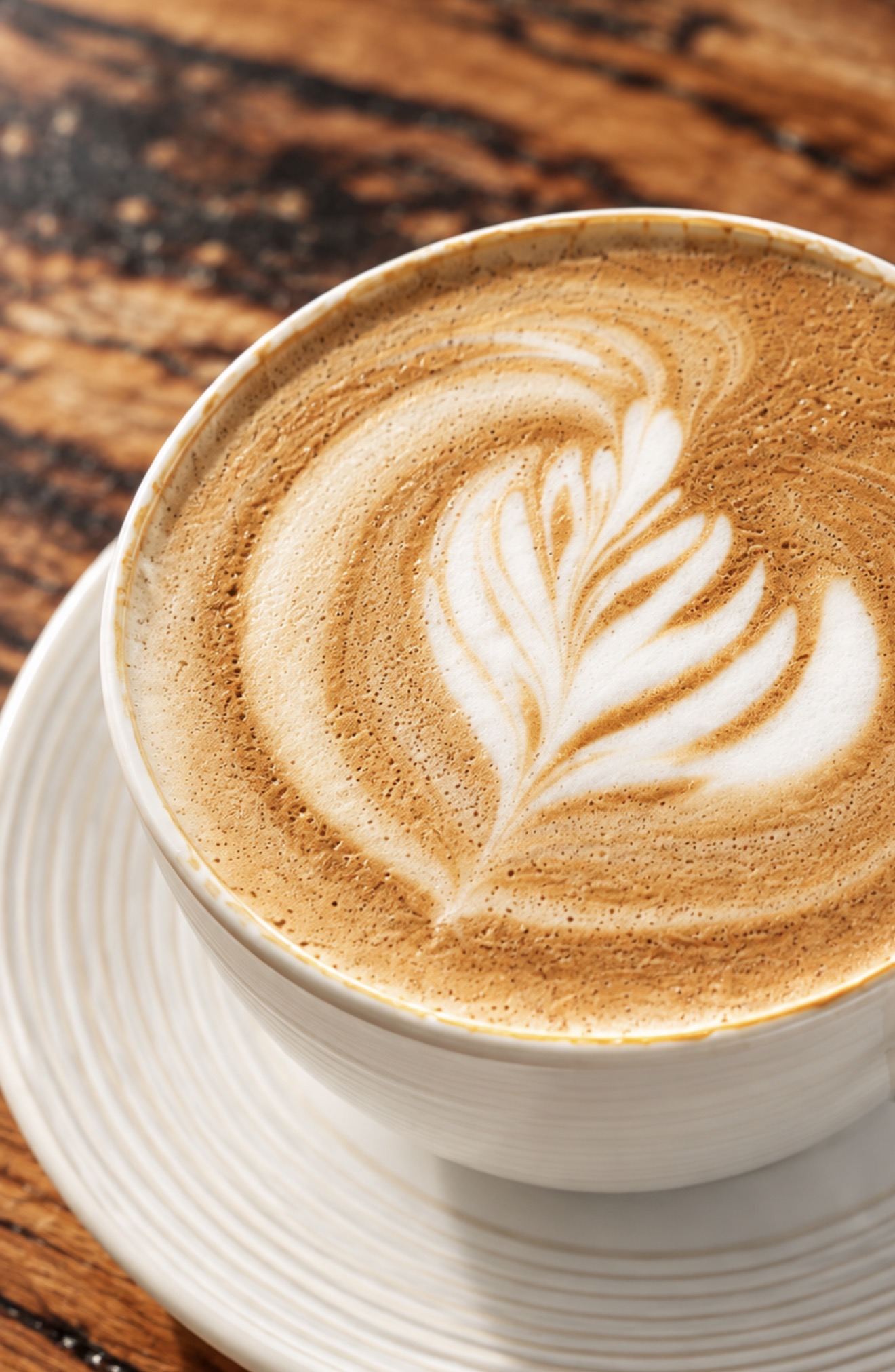 A latte with leaf art in a white cup on a wooden table