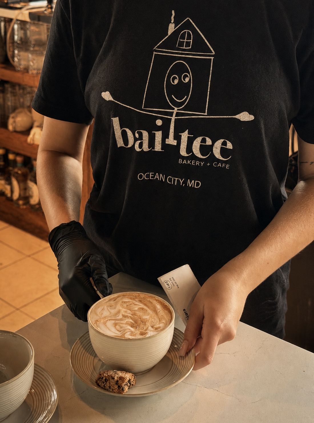 A bai-tee barista serving a cappuccino with a biscotti